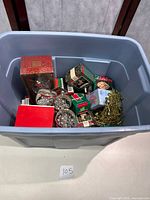 Large blue plastic bin containing various Hallmark Keepsake Christmas ornament boxes and loose items including metallic decorations.