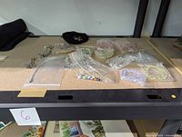 Overall view of multiple bracelets including metal charm bracelets, beaded bracelets in plastic packaging, arranged on a display surface.