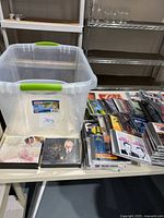Plastic storage bin and a large assortment of music CDs and audiobooks spread on a table.