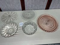 Five glass items on table: pink Depression glass platter, various clear pressed glass bowls and platters