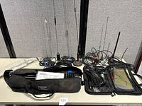 Full display of assorted antennas including long whip antennas, coiled cables, and Buddipole antenna bag and accessories laid out on table.