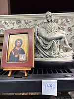 Photo showing the small framed print of Jesus with burgundy frame on an easel next to white Pieta sculpture on black base.
