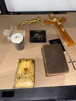 Photo showing all religious items together: two pocket bibles, wooden wall cross with brass Christ figure, brass cross, turquoise cross necklace, Easter 2018 marble cross, and small container with beads.