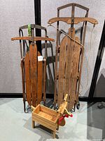 Two vintage wooden sleds shown upright with metal runners and wooden slats, one labeled 'Speedster', along with a small Rudolph wooden decorative box shaped like a sleigh with reindeer head.