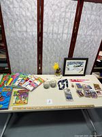 Table with puzzle books, two small New England Patriots glasses, framed print, sports pass on lanyard with pin, trading cards, Steelers bobblehead, pins and sticker arranged for display.