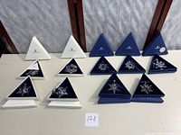 Ten triangular boxes (some closed, some open) arranged in two rows showing clear crystal star ornaments in navy velvet interiors.