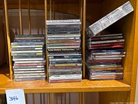 Front view of three stacks of assorted used music CDs placed on a wooden shelf including a large box set of Bruce Springsteen & The E Street Band live recordings on top right.