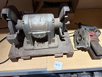 Side angle view of vintage Craftsman bench grinder on metal base and large metal bench vise side by side