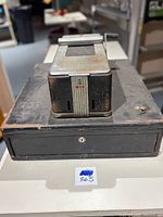 Top front angle showing the black metal cash register with the locking drawer and the metal section on top with rust.