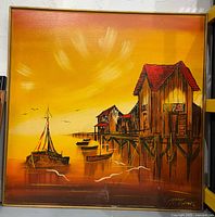 Full view of the framed painting showing seascape scene with boats and wooden stilt houses under a yellow-orange sky. Signed in the lower right corner. Frame shows signs of damage.