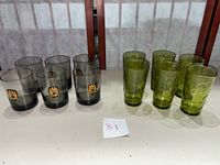 Photo showing 6 smoked glass tumblers with gold crest emblem on left, and 6 green Hazel Atlas Eldorado tumblers with raised dot pattern on right.