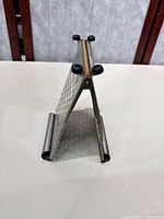 Foldable metal food grater shown unfolded with black plastic tips on feet