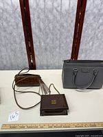 Photo showing all three handbags on a table: brown faux alligator leather roll bag with tassel and strap, brown patent leather flap bag with matching change purse, gray handbag with pink interior and detachable strap