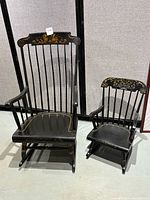 Front view of two black wooden rocking chairs, one adult and one child, with decorative floral painting on top rails and seats.