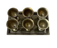 Top-down view of six brass goblets placed on a matching brass tray showing the cup interiors.