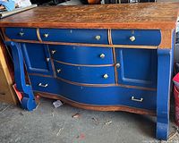 Photo showing the wooden buffet with an oak wood top and blue painted front, six drawers and two cabinet doors with unique hardware and curved design.