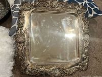 Front view of electroplated square serving tray with ornate raised decorative border and flat center surface showing scratches.