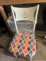 Full photo of kitchen chair showing multicolor patterned padded seat and cream metal backrest with coffee cup cut-out.