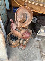 Photo showing the outdoor western fountain with a cowboy hat, saddle, barrel, and boots in a cluttered environment.