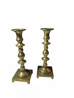 Front view of the pair of brass candleholders showing their turned column design and square bases.
