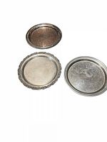 Three round metal serving trays arranged together showing distinct rim styles and ornate etching on each surface.