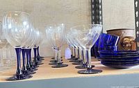 Side view showing multiple etched and plain stemmed glasses with cobalt blue stems and bases, along with cobalt blue cups and saucers stacked.