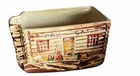 Side view of the ceramic log cabin cookie jar showing detailed log texture, red windows, painted vegetables, and door.