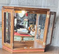 Front and side view of the vintage wood and glass display case with opened hinged doors revealing interior mirrored back and top mounted light.