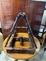 Photo showing pair of solid mahogany folding trestle supports placed on a wooden table, one open and one folded, highlighting turned leg details and polished dark wood finish.
