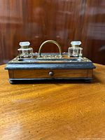 Front view of the inkwell stand showing the mahogany base, brass handle, two glass inkwells with stoppers, and drawer beneath.