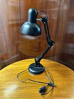 Full view of black articulated desk lamp on a wooden table with visible on/off power cord.