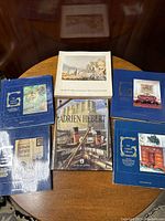 Top view of 9 books arranged on a round table; four volumes with blue covers belong to the Garbisch Collection sales, Adrien Hebert monograph in the center, and other art books