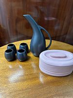 Overall shot of black ceramic wine jug and 4 tumblers with pink butter keep on wood table