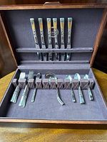 Photo of the open silverware chest showing six knives in the lid and other utensils in slots inside the chest.