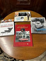 Four books displayed on a wooden round table: Danish furniture guide, Oscar Wilde book, and two Elvis Presley books including Graceland official guide and a biography.