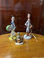Photo of three figurines: Poli For TP ceramic tambourine player, Poli For TP ceramic painter, and Hummel TMK 4 boy with bird on fence, showing relative size and condition.