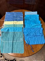 14 flatware bags and silverware keepers laid out on a table in shades of blue, teal, and yellow with ties and stitched pocket designs for storing utensils.
