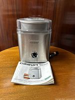 Front view of Cuisinart ice cream maker with instruction booklet shown in front on round wooden surface.
