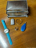 Lot overview showing Meriden silver-plated jewelry box, blue Swatch watch with cut strap, gold filled bracelet, silver plated ring, and two small perfume flasks