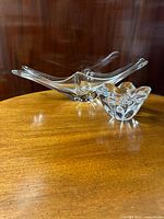 Two clear crystal pieces on wood table: an elongated oblong centerpiece and a smaller star-shaped ashtray.