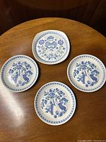 Top-down view of four Turi Design Lotte plates showing three dessert plates and one salad plate arranged on a wooden surface.