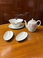 Full set of porcelain items displayed on wooden surface: two leaf shaped nut dishes, one gravy boat with underplate, and one floral coffee pot.