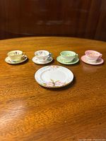 Four miniature cups and saucers displayed with a small porcelain plate on wooden surface.
