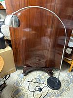 Full view of arc floor lamp showing stainless steel curved arm, silver perforated metal shade, black marble base on patterned rug.