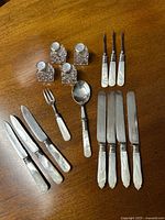 Photo showing complete set of 16 items including crystal salt and pepper shakers with sterling tops, mother of pearl-handled nut picks, dessert knives, a sugar spoon, lemon fork, and fruit cutting utensils