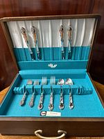 Flatware arranged in the open walnut chest showing the ornate design and satin-lined lid.