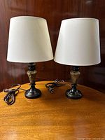 Pair of metal base lamps with faux stone finish and off-white fabric shades on wooden table.