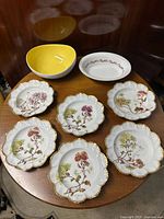 Top view of six hand-painted Limoges scalloped plates arranged around two oval bowls. Plates show floral designs with gold trim.