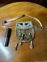 Scottish sporran made of leather and fur with silver-plated tassels alongside a metal Otis King's pocket calculator.