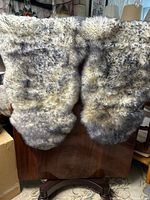 Pair of white sheepskin seat covers with grey tips displayed over chair, showing fur texture and color patterns.